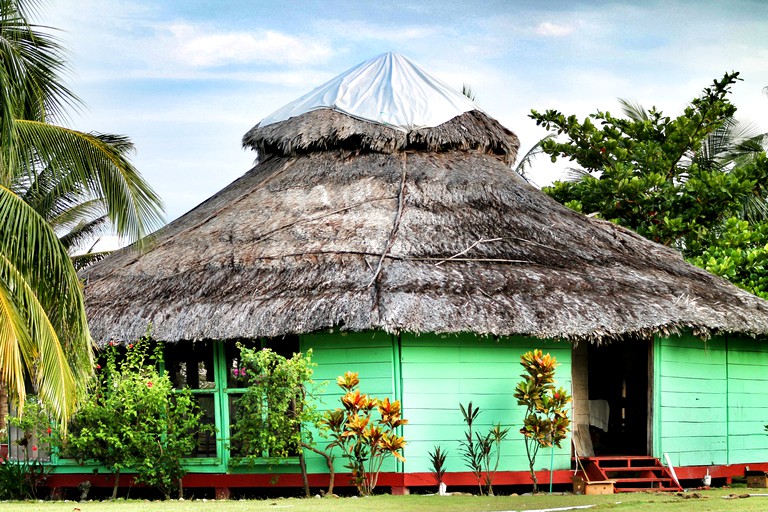 Tropical beach bungalow in Panama with green walls and thatched roof.