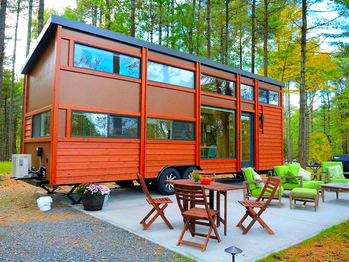 Wooden tiny house with lots of windows and patio area furnished with tables and chairs in South Cairo, New York.