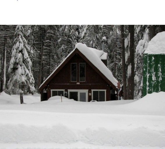 A-frame cabin rental surrounded by pine trees and covered in snow in California.